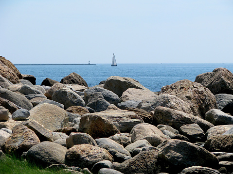 Rocky shoreline with sailboat in the background. Coast of Hammonasset Beach State Park, Madison. Connecticut.
