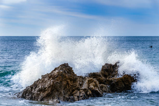 onda che si schianta sulla roccia vicino al litorale. spruzzare nell'aria; oceano dietro; cielo blu e nuvole sopra. - flowing nature spray rock foto e immagini stock