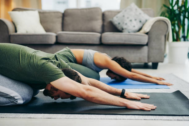 Strengthen your connection with couples yoga Shot of a young couple doing yoga together at home childs pose stock pictures, royalty-free photos & images