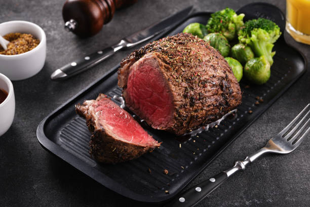 Roast beef on baking sheet with salt,  pepper and vegetables.