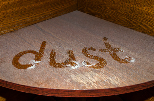 The word dust written on a dusty wooden shelf.