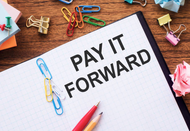istock Notebook with text PAY IT FORWARD on a table with sticks, colored paper clips and wrinkled sheets. 1304779626