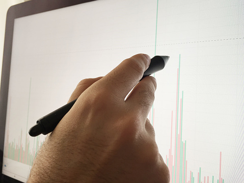 Close up hand pointing pen on computer monitor to analyzing stock market data