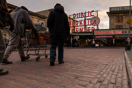Seattle, USA - Feb 25, 2021: A virtually empty Pike Place Market late in the day as three homeless pass through with a shopping cart.