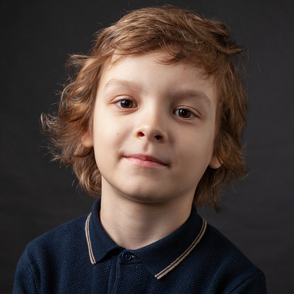 Close up studio portrait of 7 year old boy with long brown hair in polo shirt on black background
