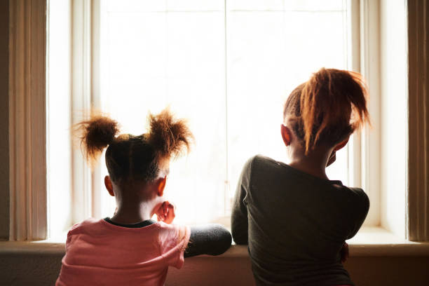 istock Little sisters looking out through a window at home 1304783163