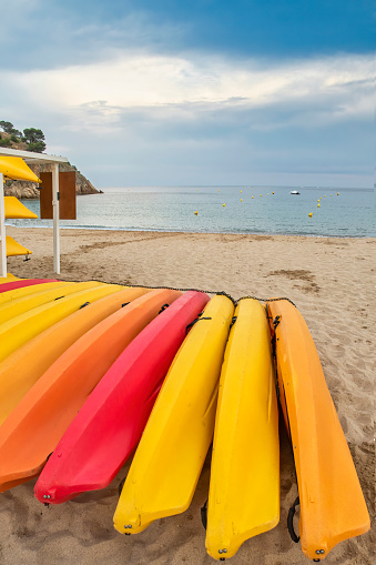 a kayak, canoe and nautical equipment rental establishment, with yellow, orange and red kayaks on the sand of a beach with crystal clear water and blue sky