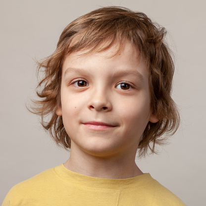 Close up studio portrait of a 7 year old boy with long brown hair in a yellow t-shirt on a beige background