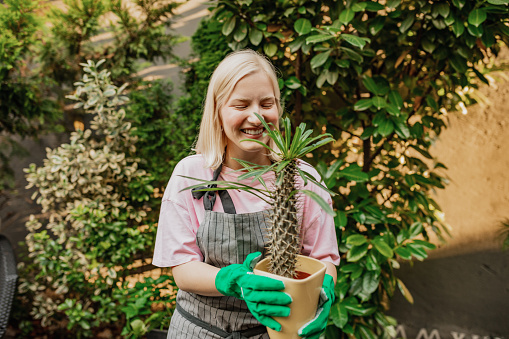 A caucasian girl is taking care of plants at her home, she is holding a plant and smiling
