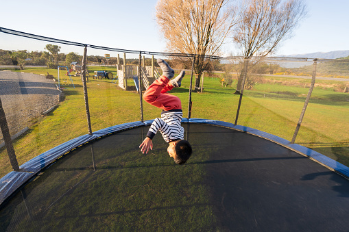 Close up of boy jumping on trampoline at day time.