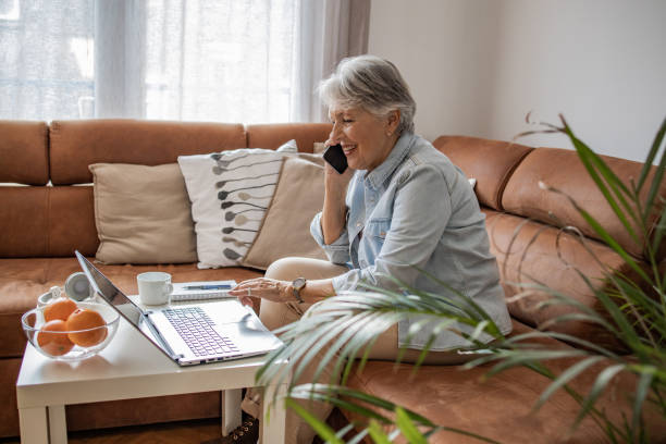 istock Senior woman talking on the phone and using laptop 1304789070