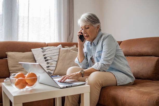 istock Senior woman talking on the phone and using laptop 1304789189