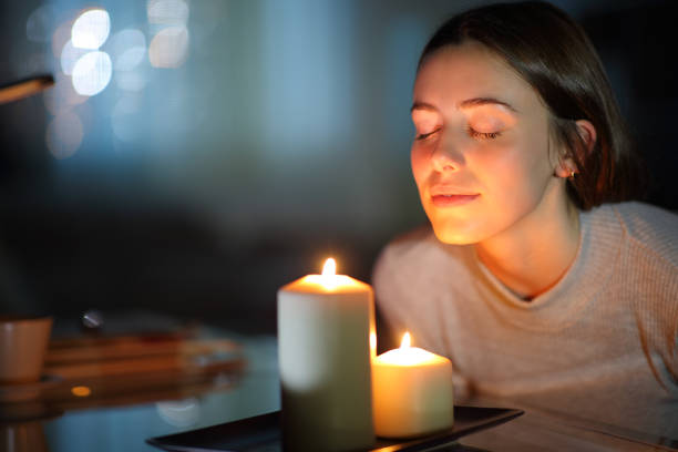 mujer oliendo una vela encendida en la noche - vela equipo de iluminación fotografías e imágenes de stock