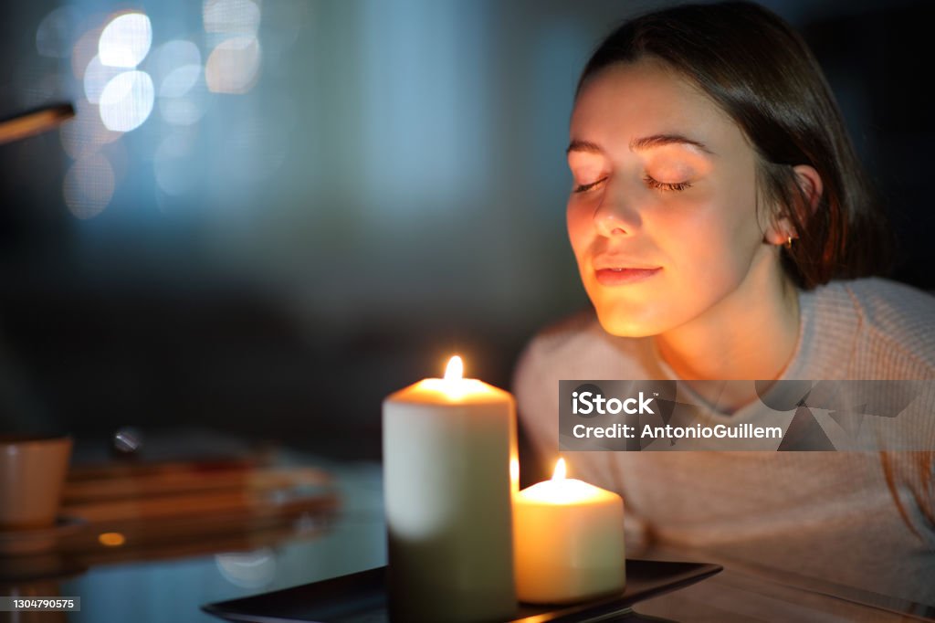 Woman smelling a lighted candle in the night Candle Stock Photo