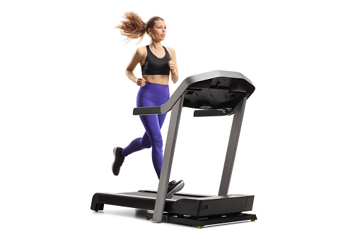 Young woman running on a treadmill machine isolated on white background