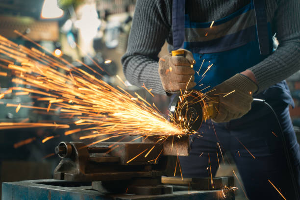 istock Locksmith in special clothes and goggles works in production. Metal processing with angle grinder. Sparks in metalworking 1304792688