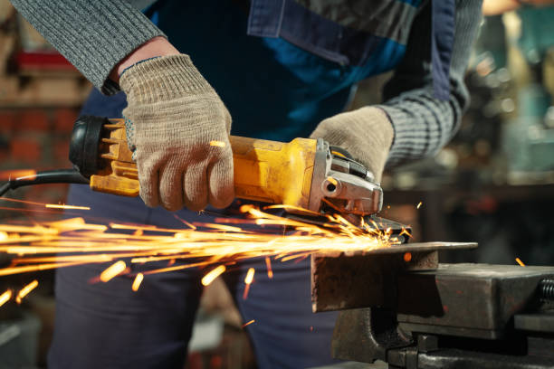 istock Locksmith in special clothes and goggles works in production. Metal processing with angle grinder. Sparks in metalworking 1304792720