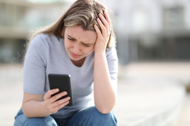 Sad teen checking bad news on mobile phone Sad teen checking bad news on mobile phone harassment photos stock pictures, royalty-free photos & images