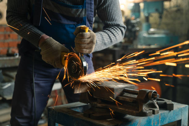 istock Locksmith in special clothes and goggles works in production. Metal processing with angle grinder. Sparks in metalworking 1304794602