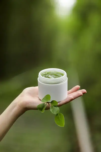 Young Female hands hold a jar of green natural cream for face or body. organic natural skincare products on green natural background. Packaging of lotion or cream. Beauty cosmetic skin care concept