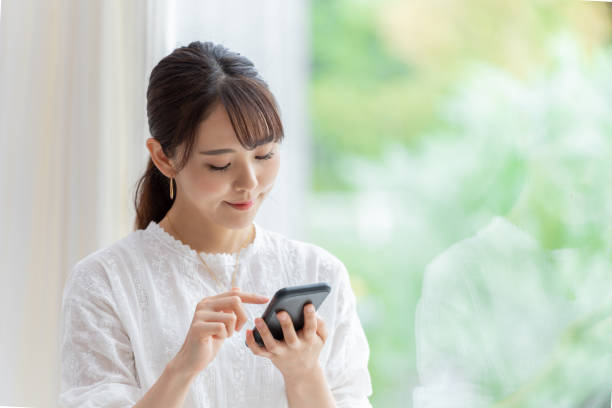 リビングルームでスマート�フォンを使用して魅力的な日本の女性 - 日本人 ストックフォトと画像