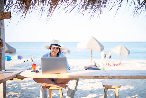 Wireless technology on the beach. Shot of a happy tourist woman sitting at the beach cafe and using a laptop. beach bar stock pictures, royalty-free photos & images