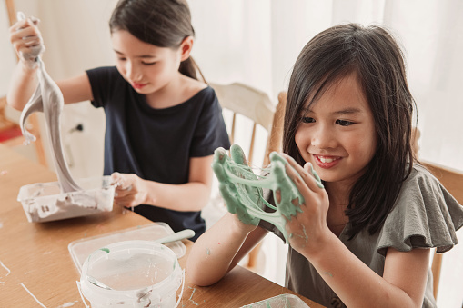 Happy mixed Asian girl friends making homemade slime toy, sensory art and craft, fun homeschool chemistry project