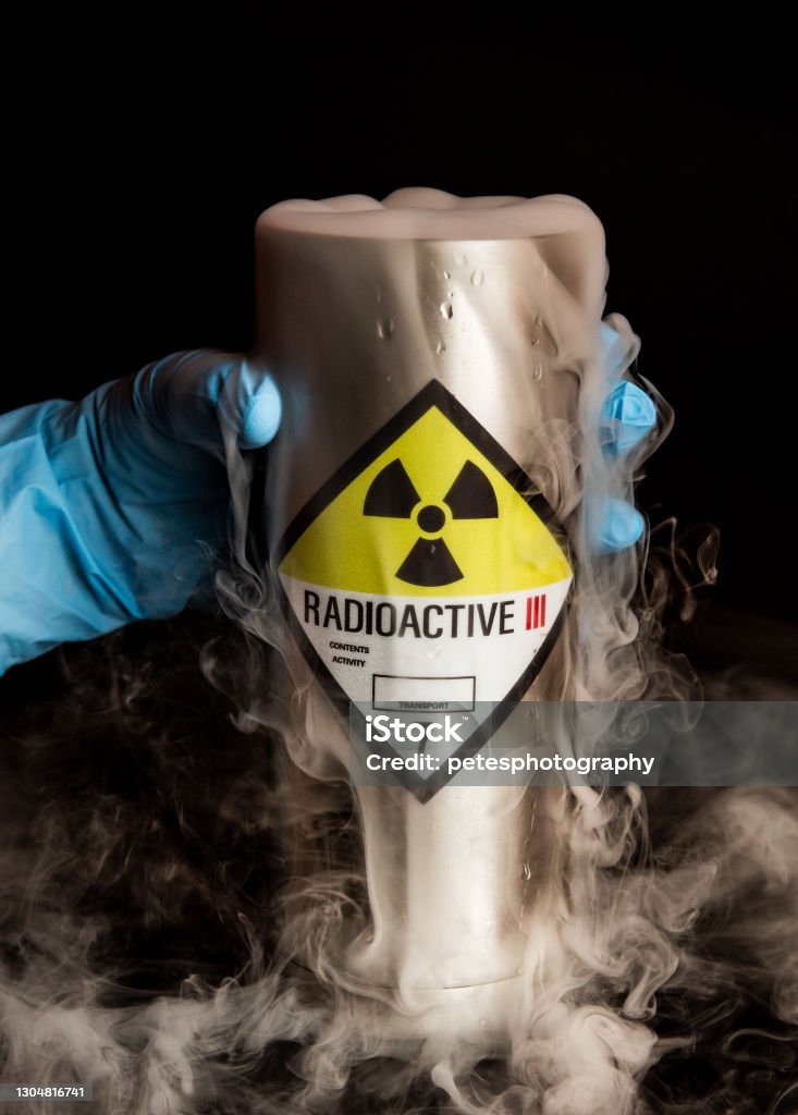 A metal radioactive canister with lots of smoke held by a hand in rubber glove A metal canister with a radioactive symbol sticker on it on a black background with smoke billowing out of it held by a hand wearing a blue protective rubber glove. Radioactive Contamination Stock Photo