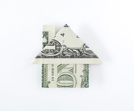 Origami dollar house on top of dollar bills on white background