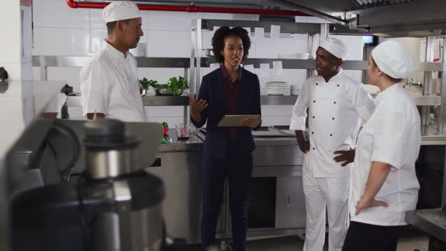 African american female manager using tablet and talking with chefs