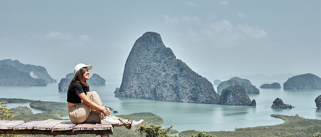 A happy Asian woman sits on a wooden bridge against the backdrop of the sea and many islands. Unseen Thailand Tourism at Samet Nangshe.