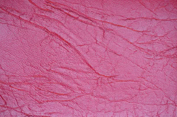 A fragment of genuine leather with wrinkles and folds, artificially dyed in a bright crimson color. Background, pattern, texture.