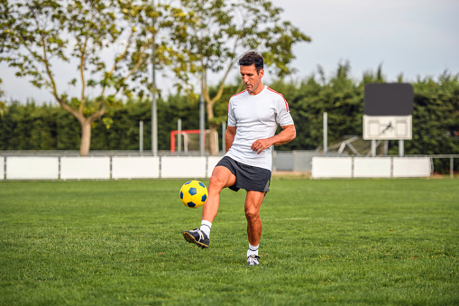 Action portrait of mature male footballer practicing ball control on sports field.