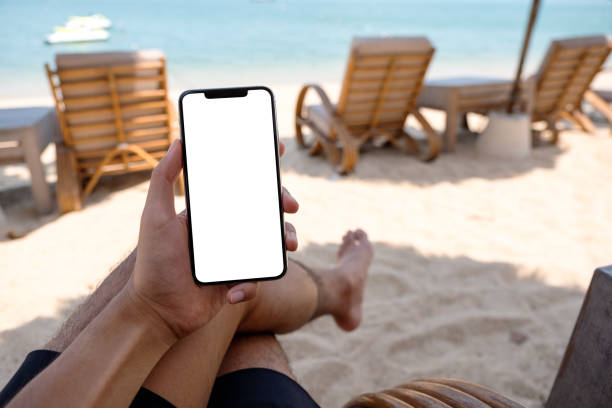 istock a man holding mobile phone with blank desktop screen while sitting on the beach 1304822611