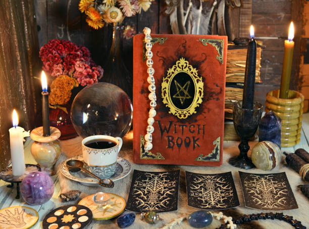 istock Red witch book with tarot cards, tea cup, black candle and magic ritual objects on the table. 1304822630