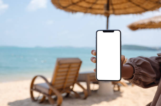 istock a woman holding and showing mobile phone with blank desktop screen while sitting on the beach 1304822637