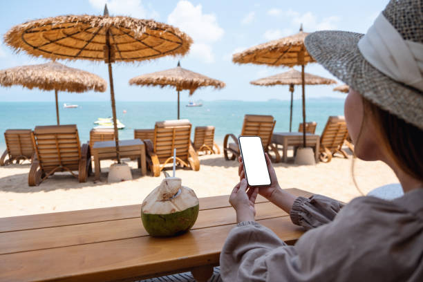 istock a woman holding mobile phone with blank desktop screen while sitting on the beach 1304822640