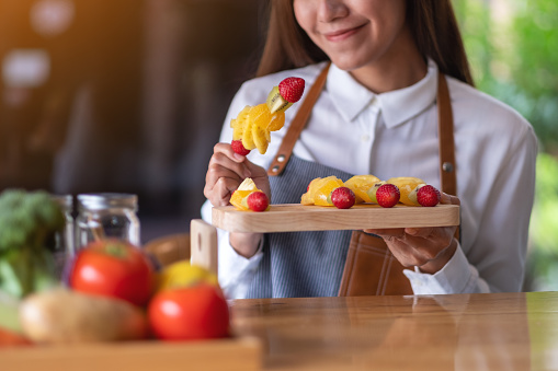 Closeup image of a beautiful female chef holding fresh mixed fruits on skewers in a wooden plate