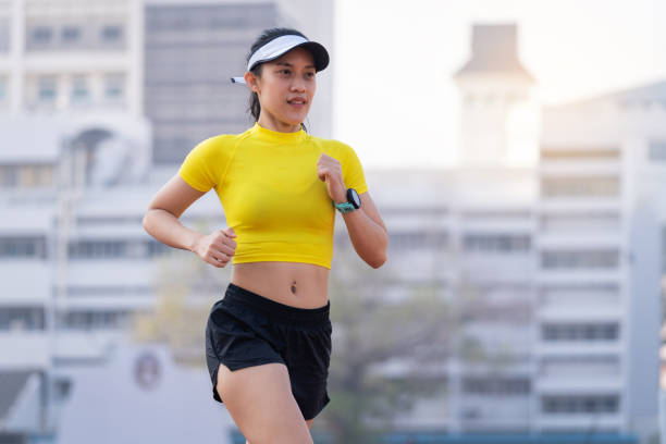 A young Asian woman athlete runner jogging on running track in city stadium in the sunny morning to keep fitness and healthy lifestyle. Young fitness woman runs on the stadium track. Sport and recreation stock photo