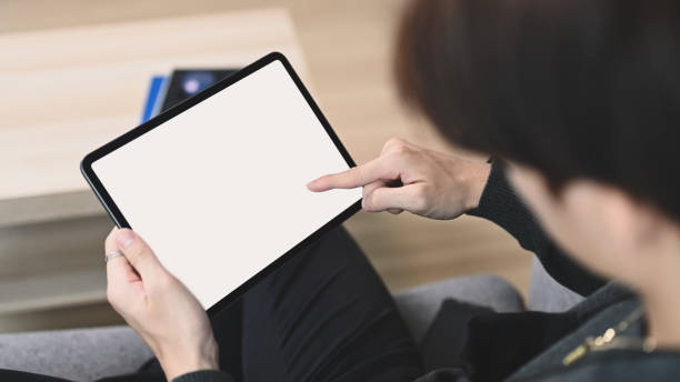istock Close up view of young man holding horizontal digital tablet with blank screen while sitting on couch. 1304832294