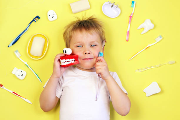 黄色の背景に歯ブラシとおもちゃの歯を保持しているかわいい男の子の子供の子供。歯のクリーニング、口腔ケア、歯科衛生概念、トップビュー。 - child brushing human teeth brushing teeth ストックフォトと画像