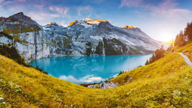 Idyllic panorama view of the lake Oeschinensee in day. Location place Swiss alps, Kandersteg, Bernese Oberland, Europe. Scenic image of most popular tourist attraction. Discover the beauty of earth.