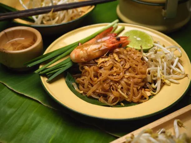 Cropped shot of stir fired Thai noodles with shrimps serving on black plate with lime, beansprouts and chives, Pad Thai