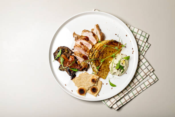 istock Duck breast with cabbage steak, cheese sauce and rye flatbread. Delicious restaurant dish on a round plate on a checkered napkin. Top view 1304841218