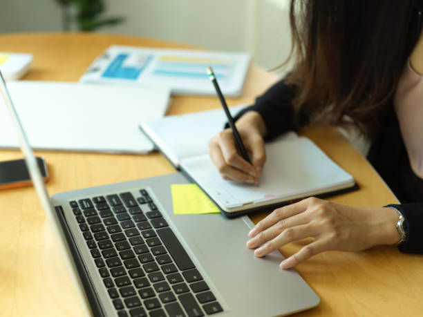 istock Businesswoman hand writing on schedule book while working with laptop 1304842182