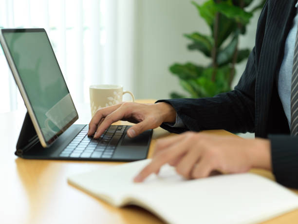 istock Businessman hand pointing on notebook and typing on tablet keyboard 1304842193