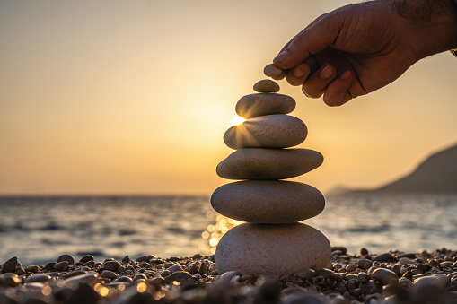 Young man's hand balancing stacking stones on a beach