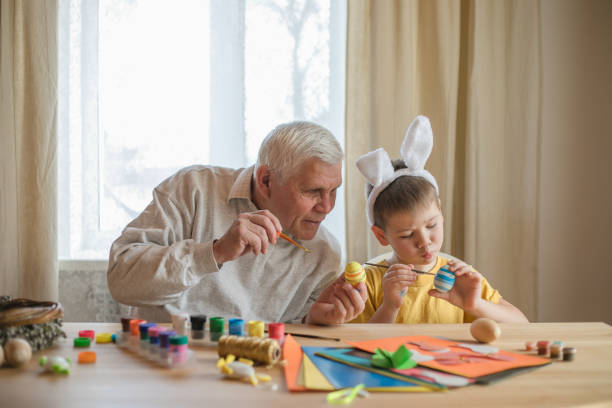 Happy elderly man granfather preparing for Easter with grandson. Portrait of smiling boy with bunny ears painted  colored eggs for Easter stock photo