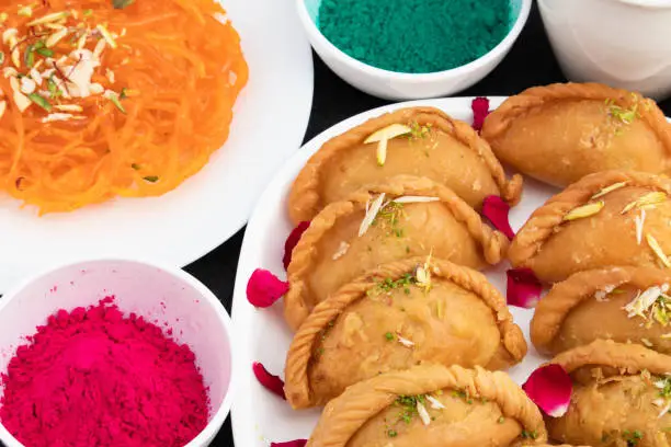 Festival Of Colors Happy Holi Celebration - Closeup Of Delicious Gujia Or Gujiya Mithai Made In Desi Ghee Dry Fruits Pista Badam Kesar Served With Jalebi Ghewar And Colorful Gulal Abeer Or Abir
