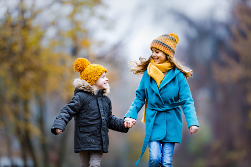 Carefree brother and sister having fun while holding hands and running in autumn day at the park. Copy space.